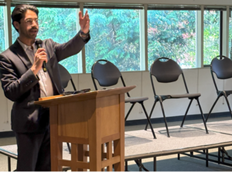 Representative Osman Salahuddin speaking at a podium during the June 2025 Eastside faith-based housing convening.